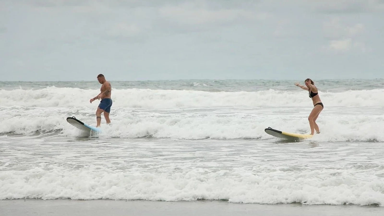A man and woman ride small whitewater waves on surfboards near shore in Nosara