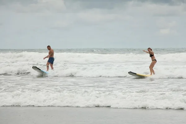 A man and woman ride small whitewater waves on surfboards near shore in Nosara