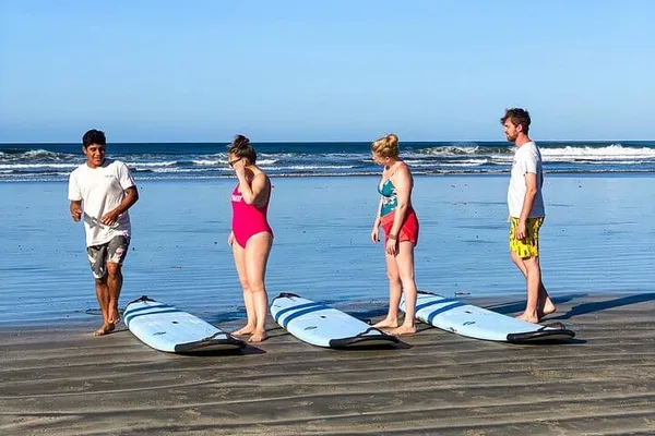 Surf instructor and three students stand beside surfboards on the beach in Nosara before a lesson
