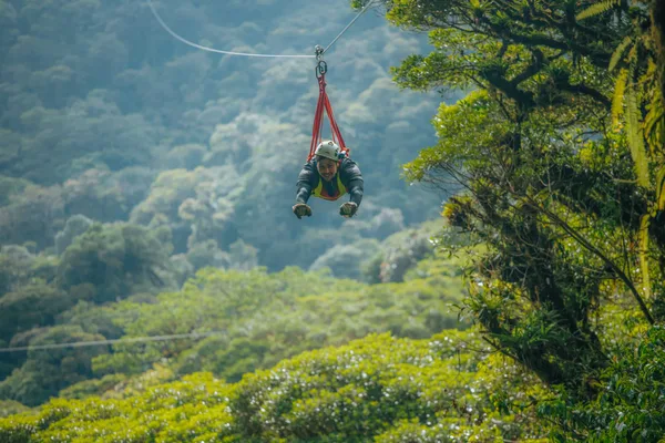 A zipliner in a superman-style harness soars over the lush forest canopy in Monteverde
