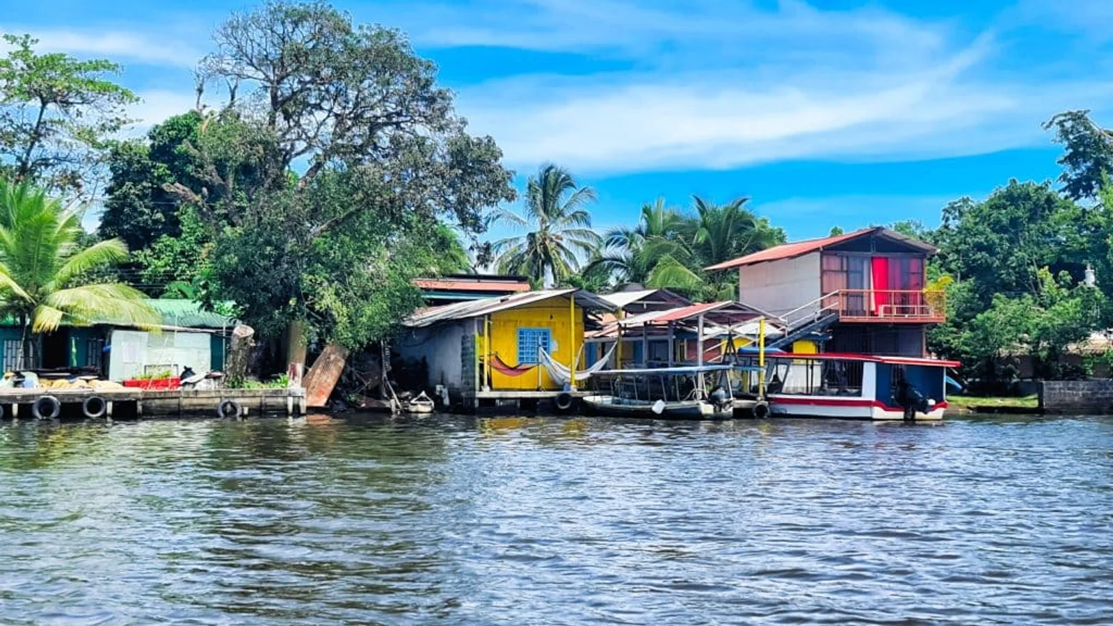 Riverside houses on stilts with docked boats along a waterway in Tortuguero, surrounded by trees