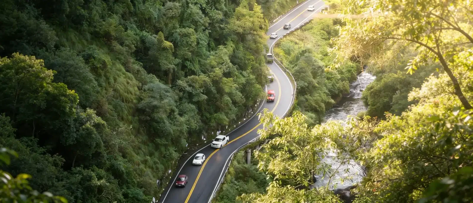 Aerial view of cars winding along a curvy forested mountain road beside a stream in Costa Rica