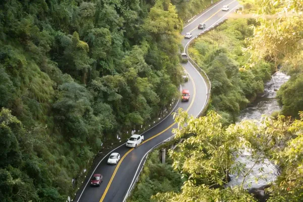 Aerial view of cars winding along a curvy forested mountain road beside a stream in Costa Rica