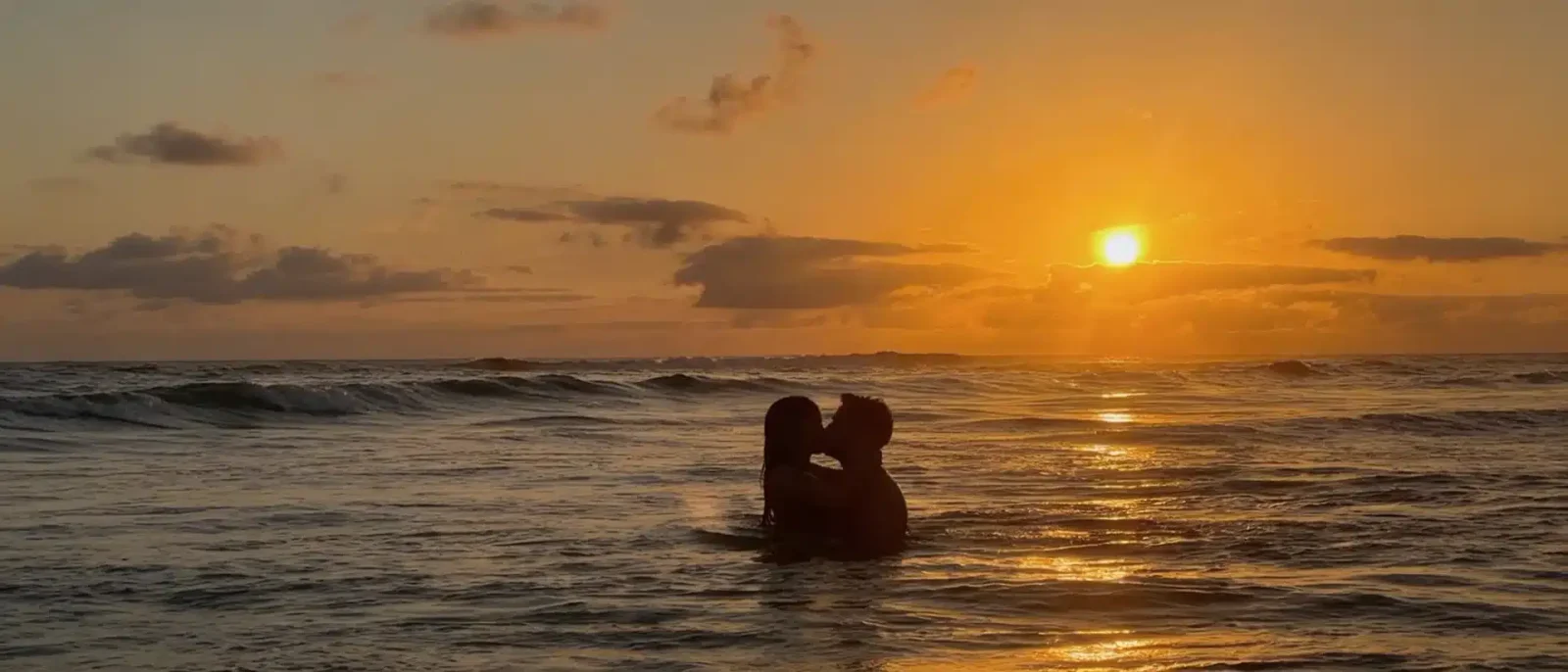 Couple embracing in the ocean silhouetted against a golden sunset