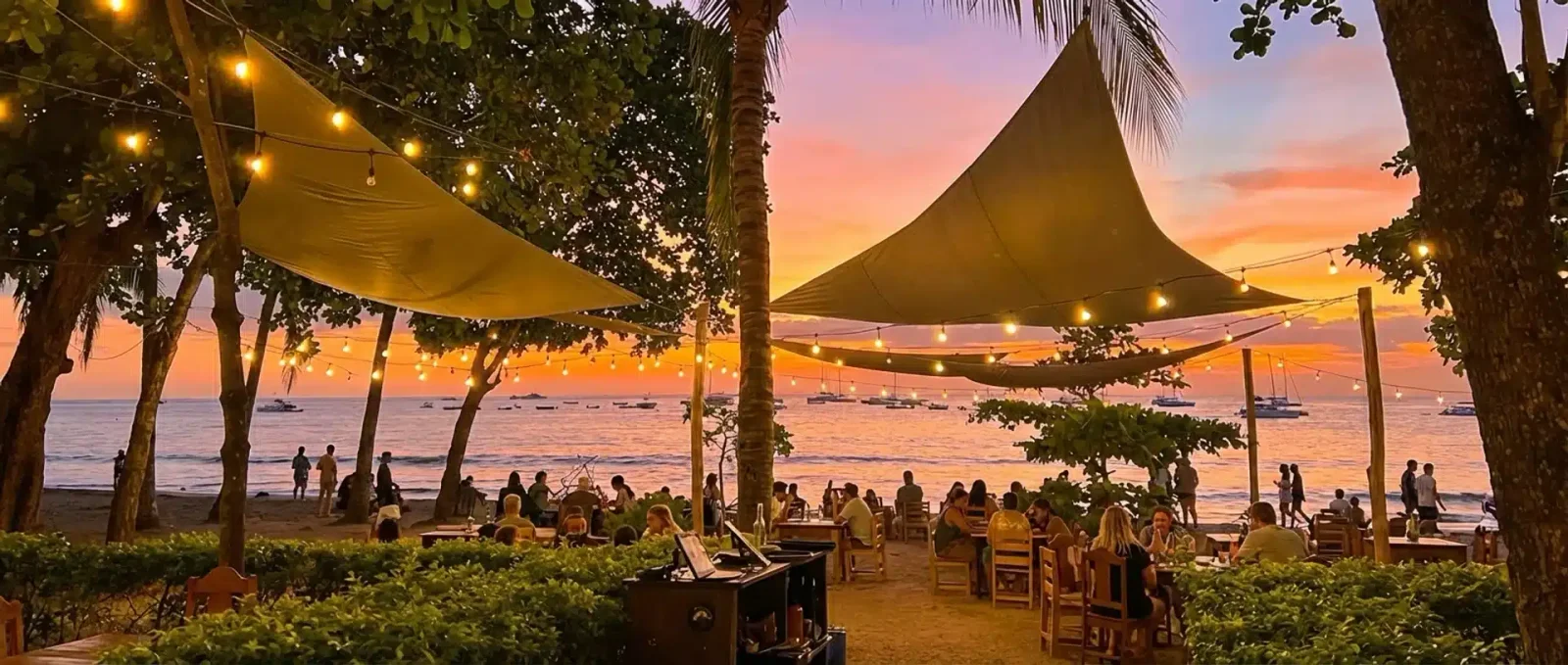 Beachfront restaurant in Tamarindo with sail shades and string lights at sunset, ocean and boats behind