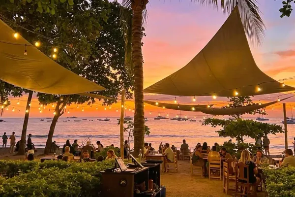 Beachfront restaurant in Tamarindo with sail shades and string lights at sunset, ocean and boats behind