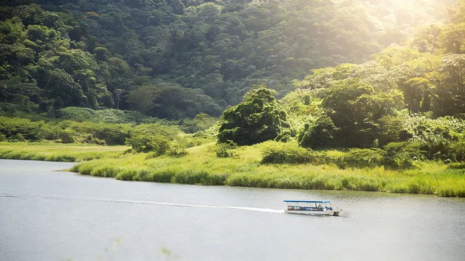 A small tour boat crosses a river beneath forested hills near Lake Arenal, Costa Rica