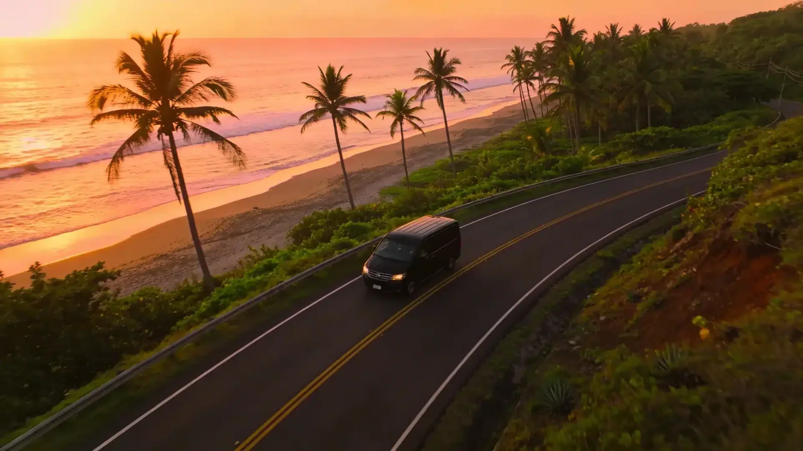 A van drives along a coastal road lined with palm trees at sunset in Costa Rica