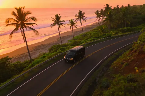 A van drives along a coastal road lined with palm trees at sunset in Costa Rica
