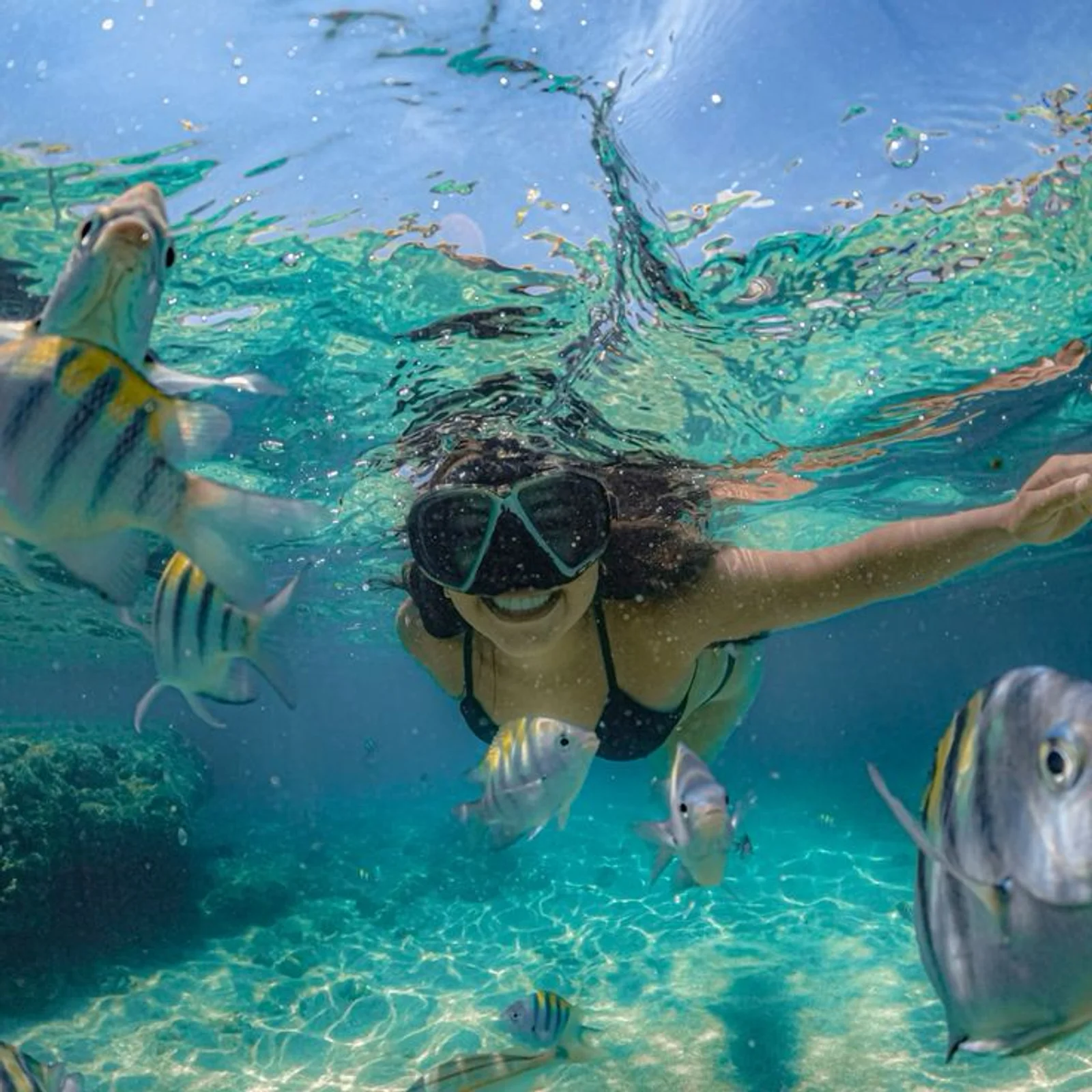 Woman snorkeling underwater with a mask, smiling as tropical fish swim around her