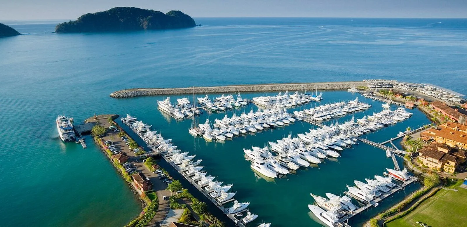Aerial view of Los Sueños Marina with rows of docked yachts and boats, ocean and islands beyond