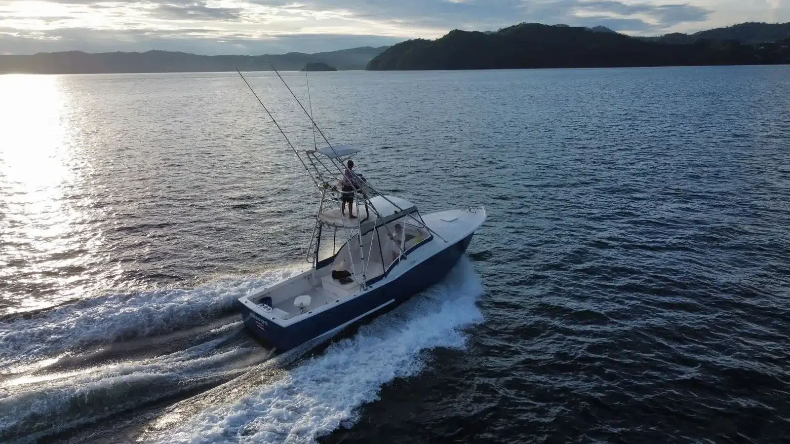 Sport fishing boat with tower cruising across the Gulf of Papagayo, leaving a wake at sunset