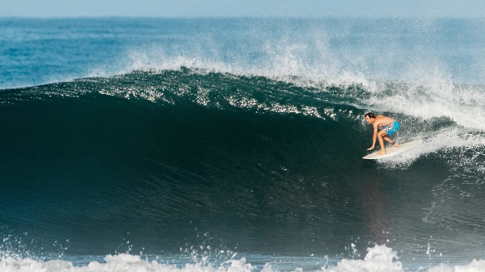 A surfer crouches low riding a large curling wave in Santa Teresa, Costa Rica