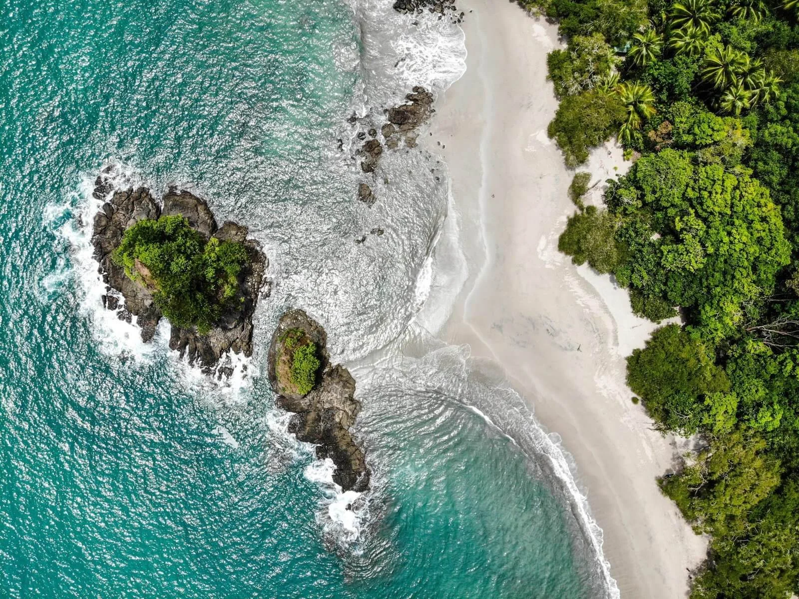 Aerial view of rocky islets, turquoise waves, white sand beach and rainforest at Manuel Antonio