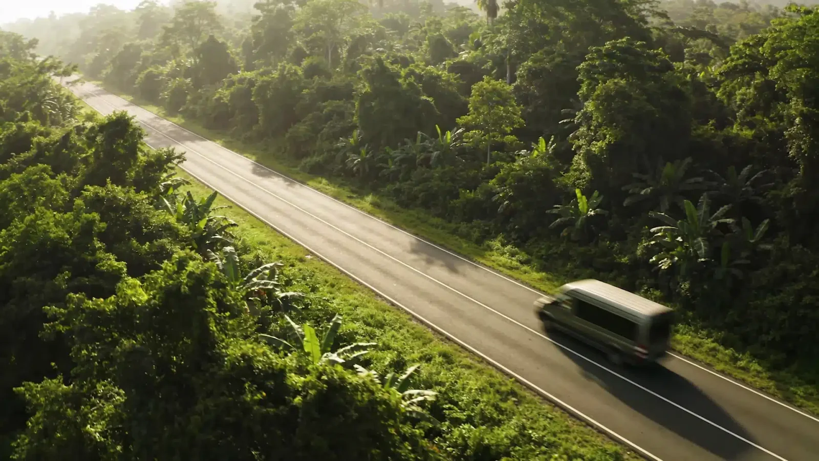 A van drives along a rural highway through lush green jungle in Costa Rica