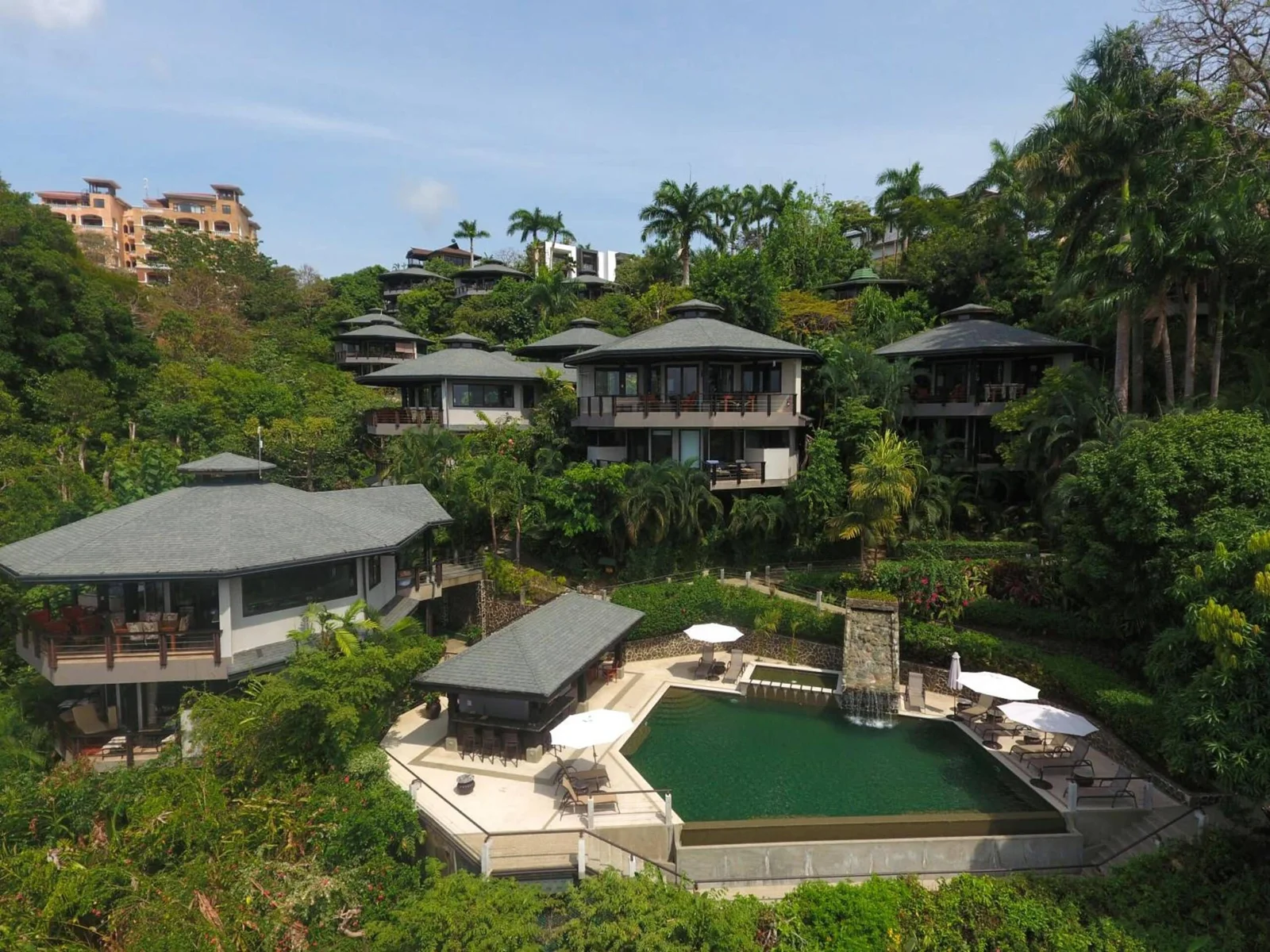 Aerial view of a hillside resort with pool, umbrellas, and villas surrounded by tropical jungle