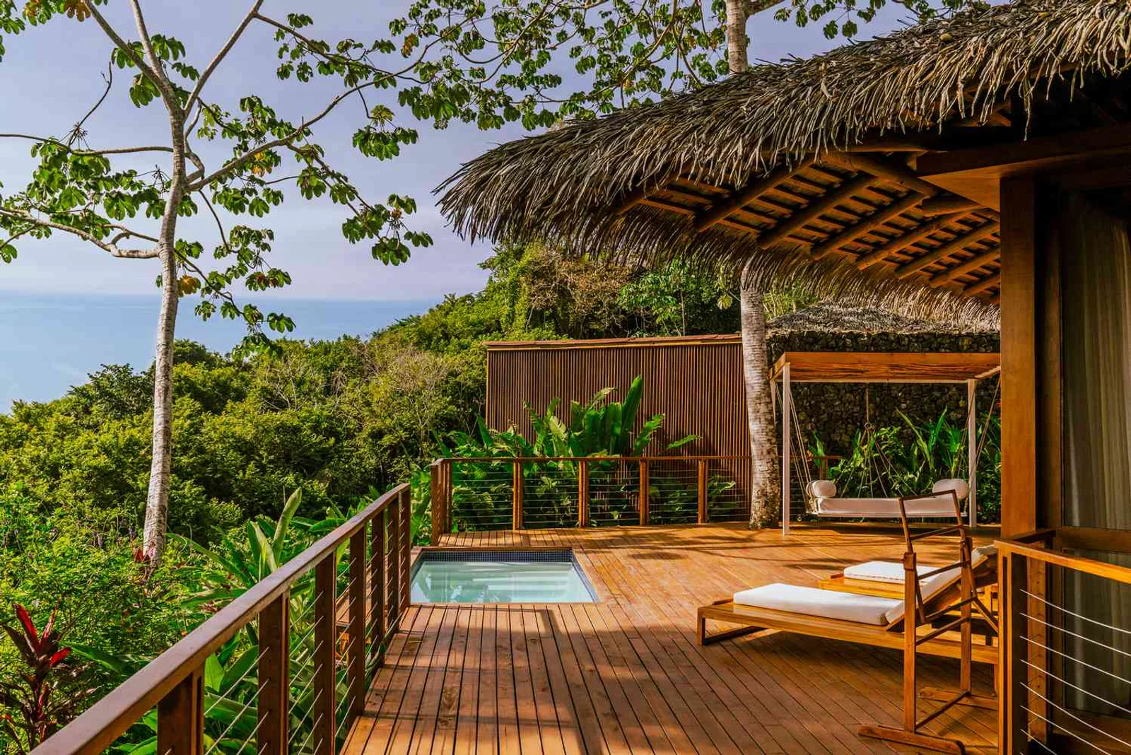 Thatched-roof villa deck with a plunge pool, lounge chairs and swing overlooking a jungle canopy