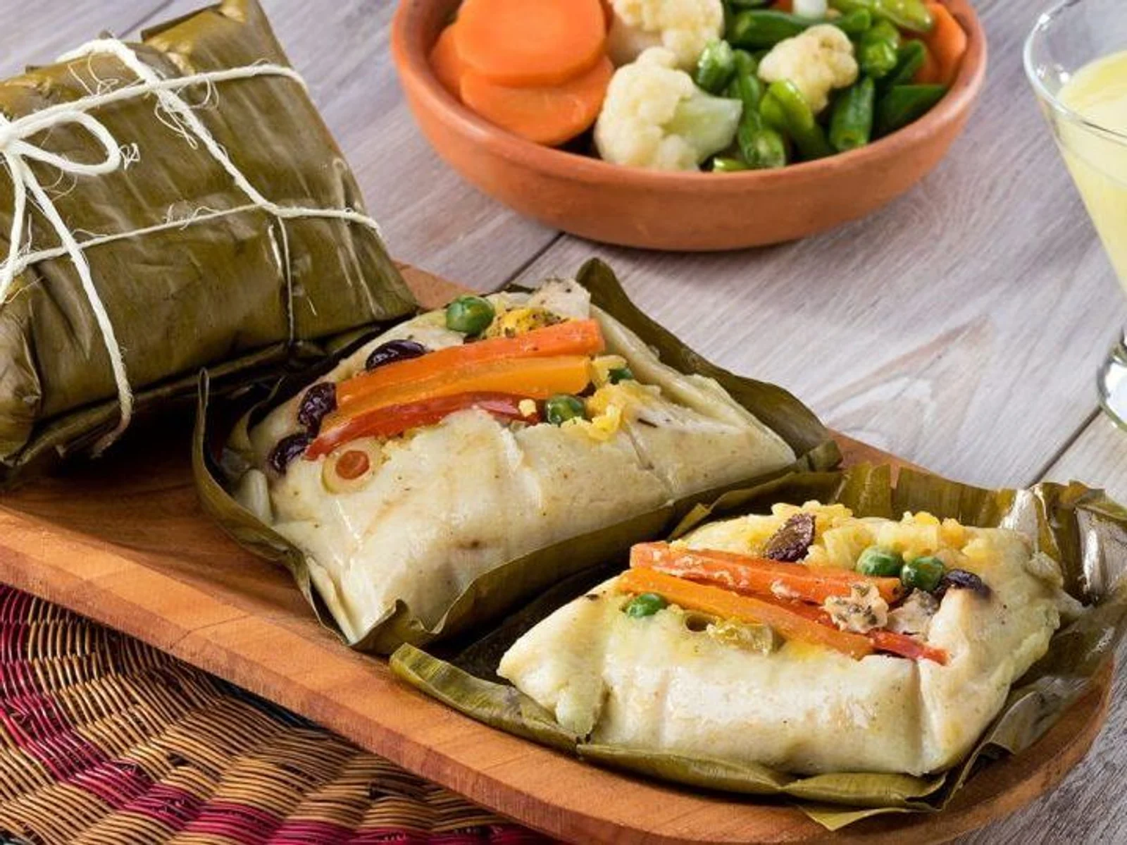 Costa Rican tamales wrapped in banana leaves, served with a bowl of steamed vegetables