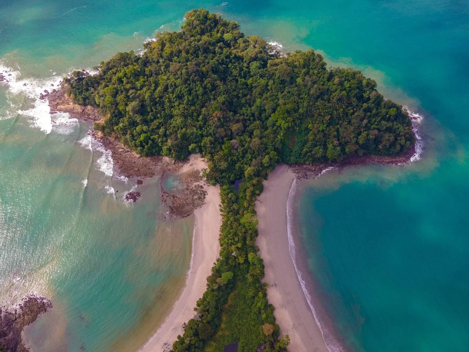 Aerial view of a forested headland with a tombolo sandbar connecting it to the coast at Manuel Antonio National Park