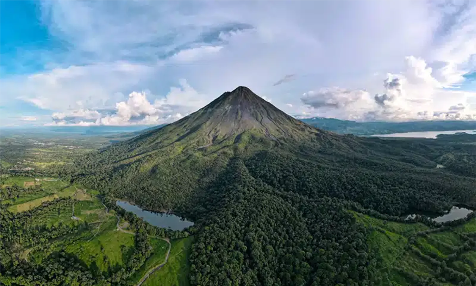 Aerial view of Arenal Volcano's cone rising above lush rainforest and lakes in La Fortuna, Costa Rica