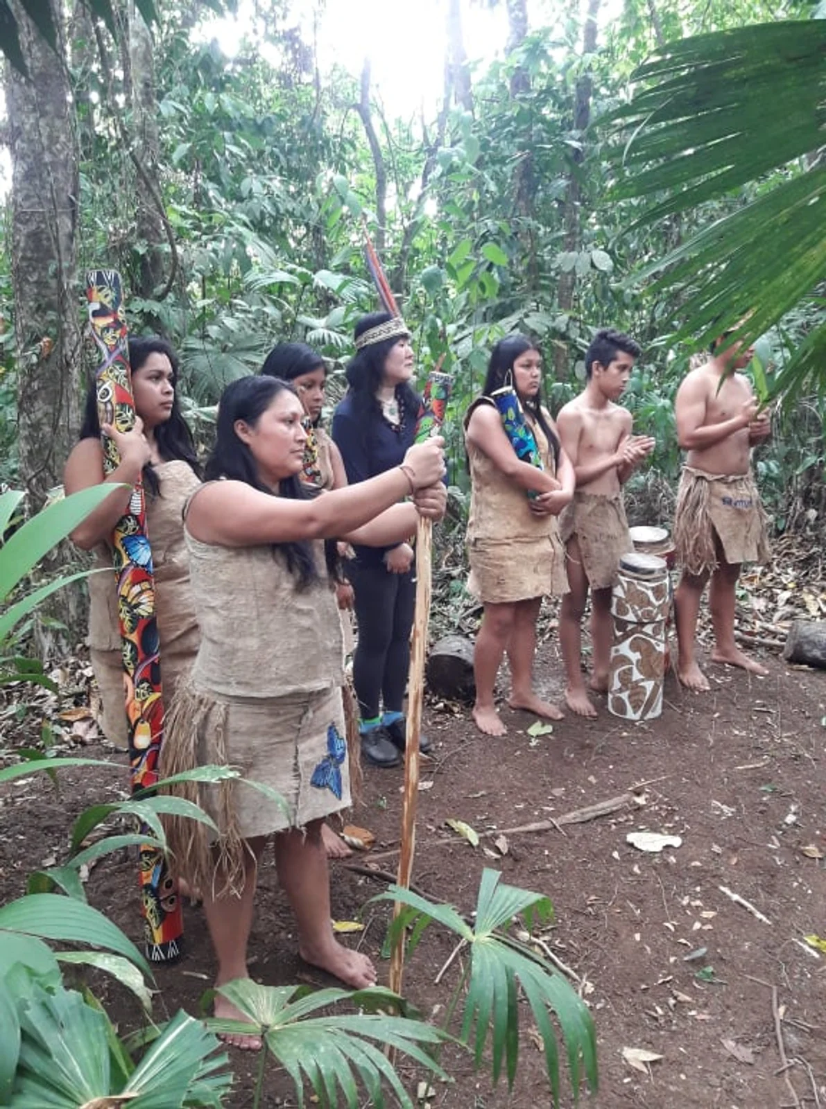 Indigenous group in traditional bark cloth and grass skirts stands in the forest during a cultural ceremony