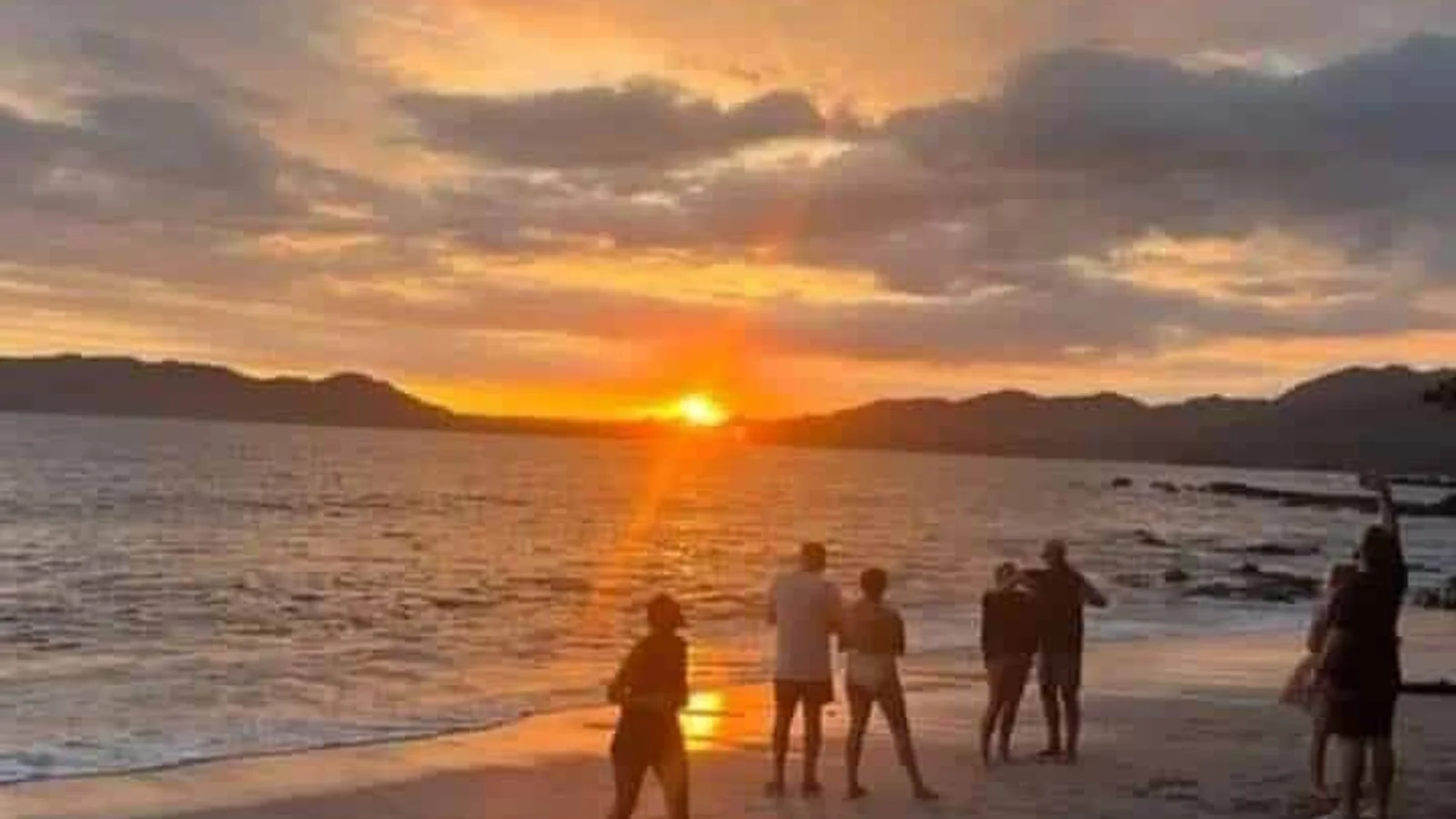 Silhouetted people watching a vivid orange sunset over the ocean from a beach in Santa Teresa