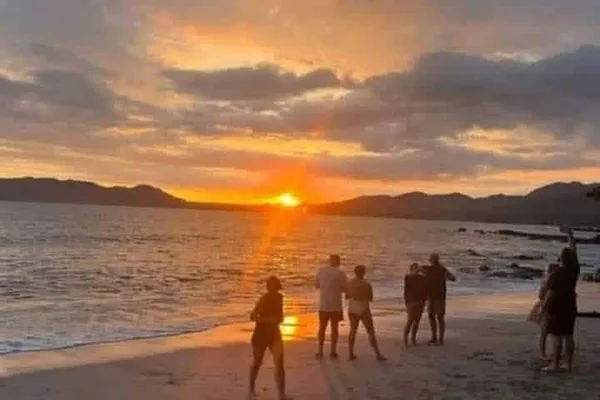 Silhouetted people watching a vivid orange sunset over the ocean from a beach in Santa Teresa