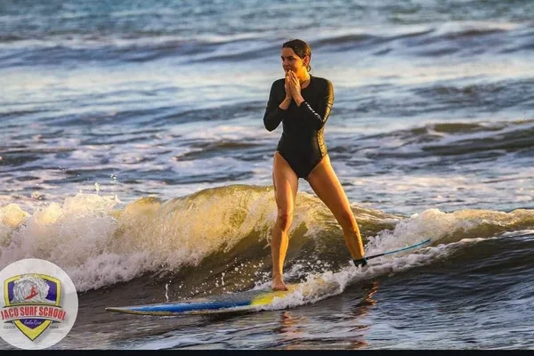 Woman in a black wetsuit riding a small wave on a surfboard in Jaco, Costa Rica