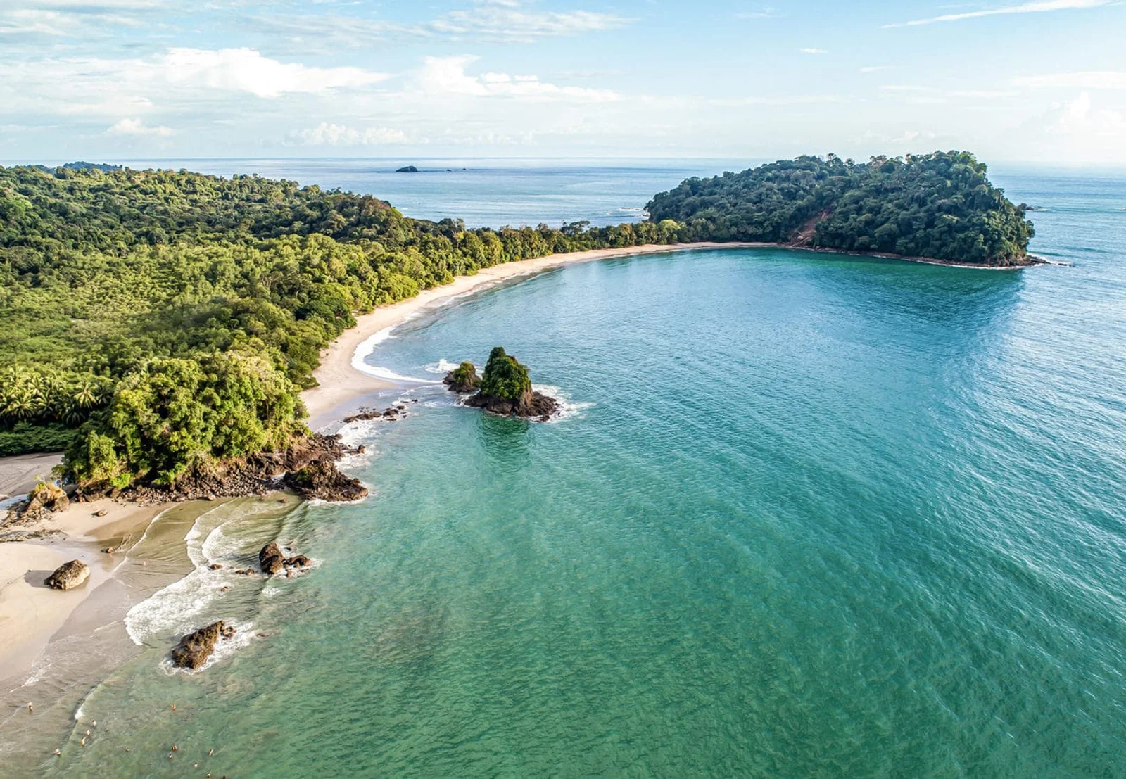 Aerial view of a curved sandy beach, turquoise cove and forested headlands in Manuel Antonio