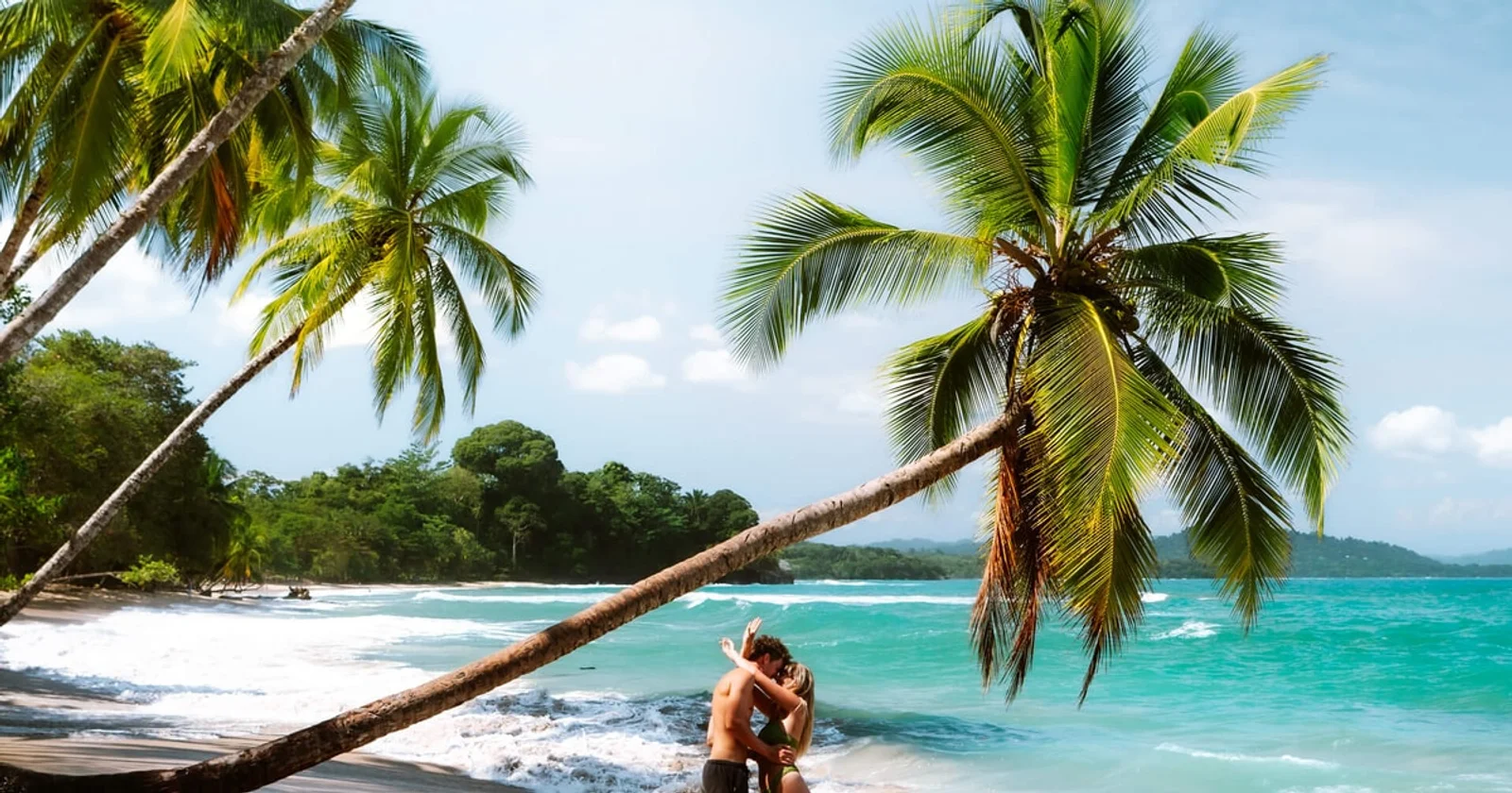 Couple embracing on a tropical beach beneath leaning palm trees with turquoise water
