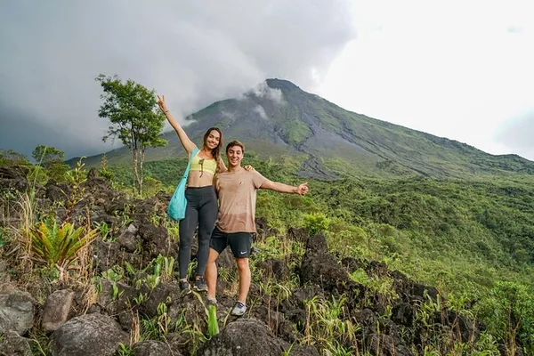 Couple posing on volcanic rocks with Arenal Volcano rising behind them under cloudy skies