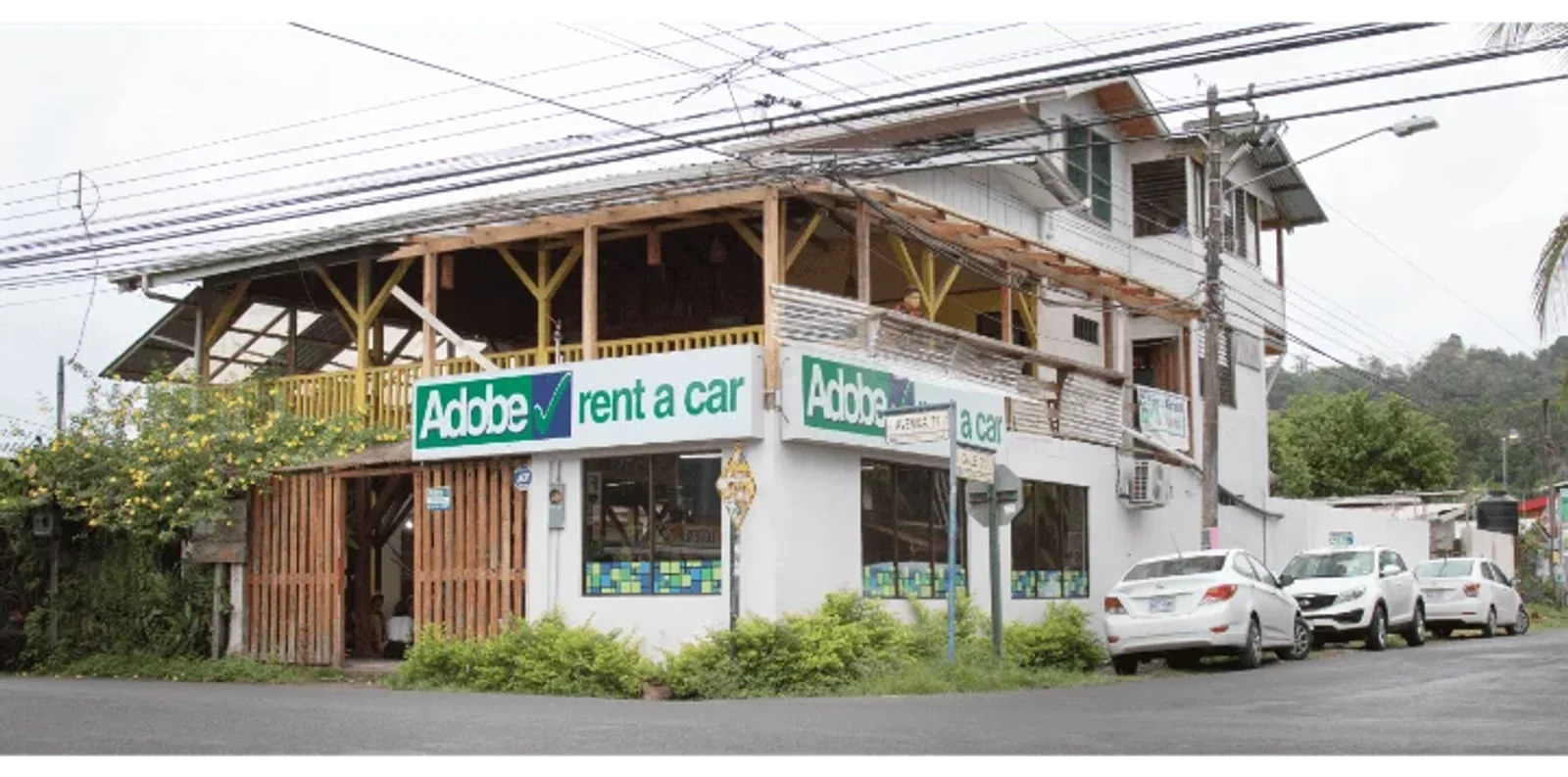 Adobe Rent a Car storefront in a wooden two-story building with parked cars out front
