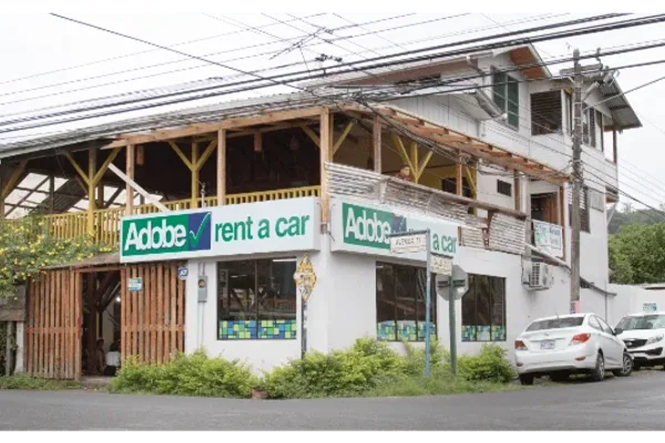 Adobe Rent a Car storefront in a wooden two-story building with parked cars out front