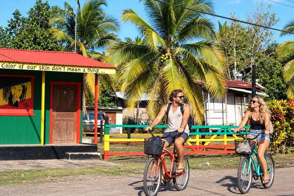 Couple riding cruiser bicycles past a colorful Rasta-painted building with palm trees in Puerto Viejo