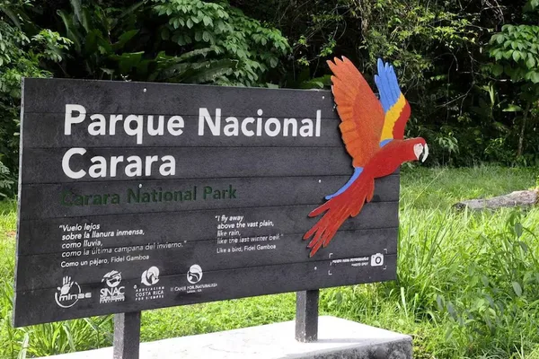 Entrance sign for Carara National Park with a colorful scarlet macaw decoration, surrounded by greenery