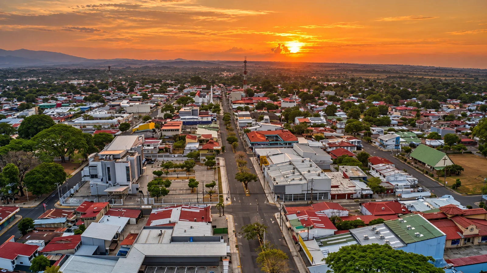 Aerial view of a Liberia, Costa Rica town at sunset with rooftops, a main street, and mountains in the distance