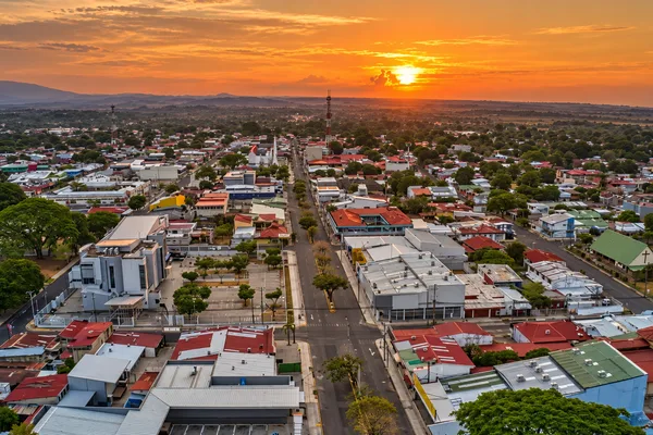 Aerial view of a Liberia, Costa Rica town at sunset with rooftops, a main street, and mountains in the distance