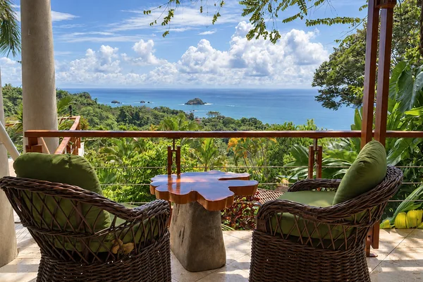 Wicker chairs and a wooden table on a jungle-view balcony overlooking Manuel Antonio's coastline