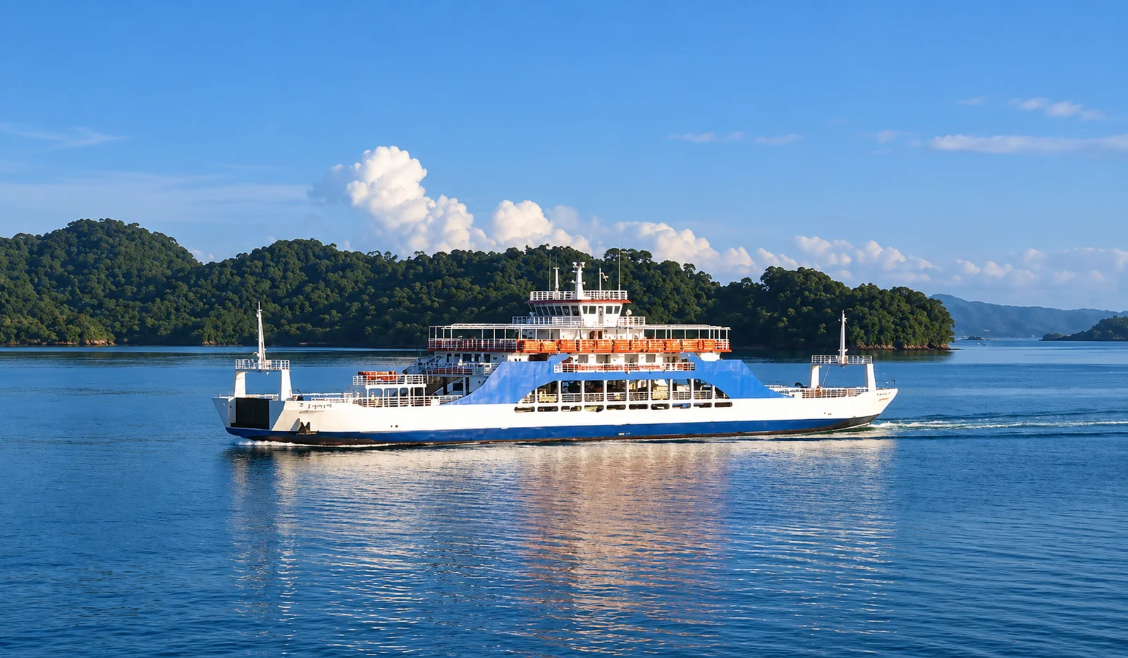 A car ferry crosses calm blue water with forested islands and hills in the background