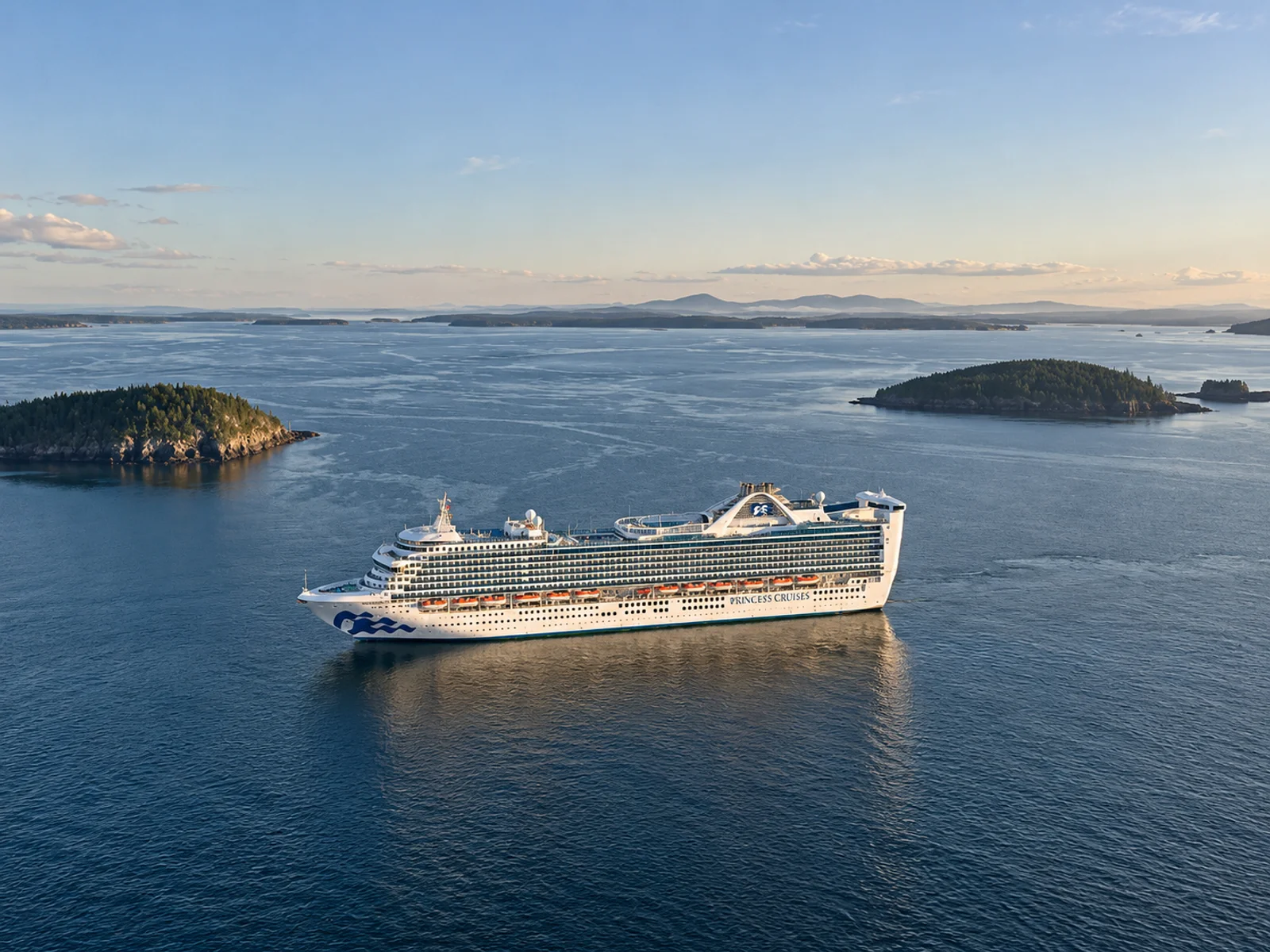 A Princess Cruises ship anchored near forested islands in a calm bay at dusk