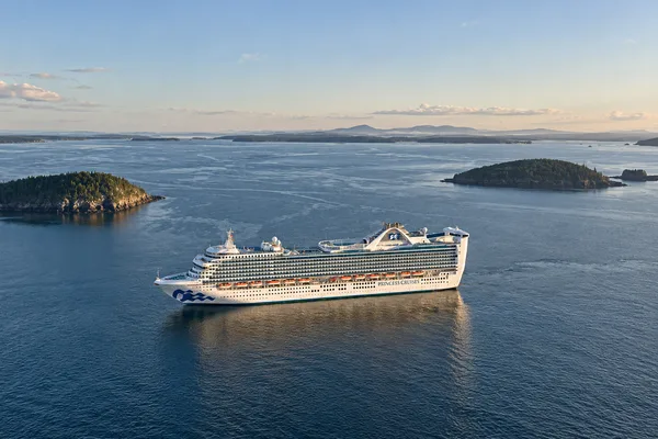 A Princess Cruises ship anchored near forested islands in a calm bay at dusk