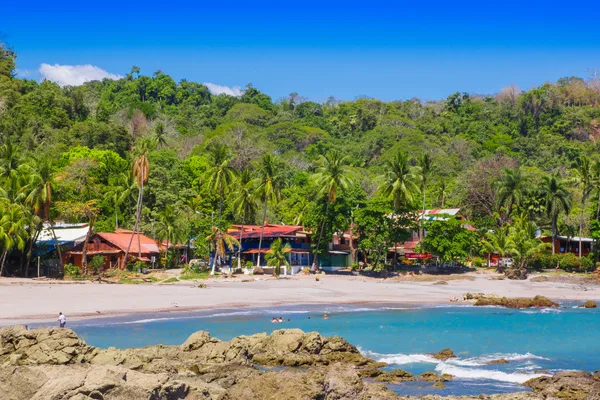 Rocky shoreline overlooking a beach town lined with palm trees and a jungle-covered hillside in Montezuma, Costa Rica