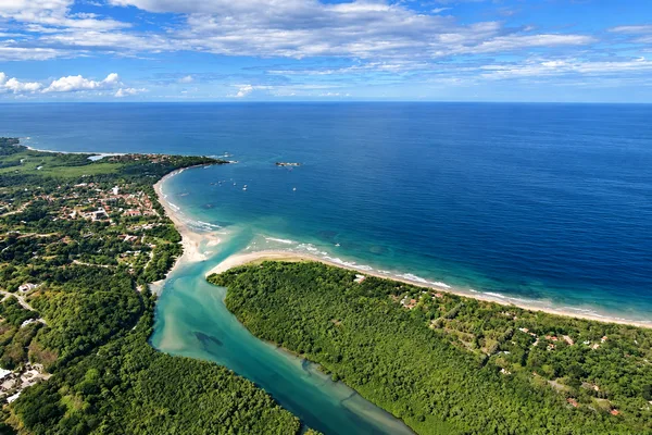 Aerial view of a coastal river mouth meeting the ocean beside a beach town with green mangroves