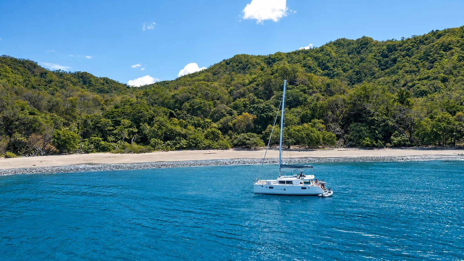 Catamaran anchored near a sandy beach in Papagayo Gulf, with forested hills behind and turquoise water