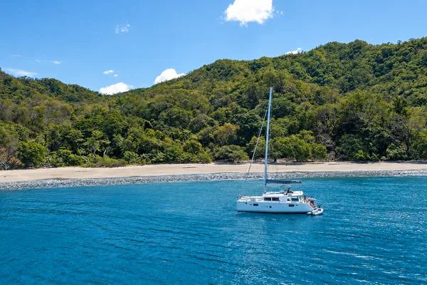 Catamaran anchored near a sandy beach in Papagayo Gulf, with forested hills behind and turquoise water