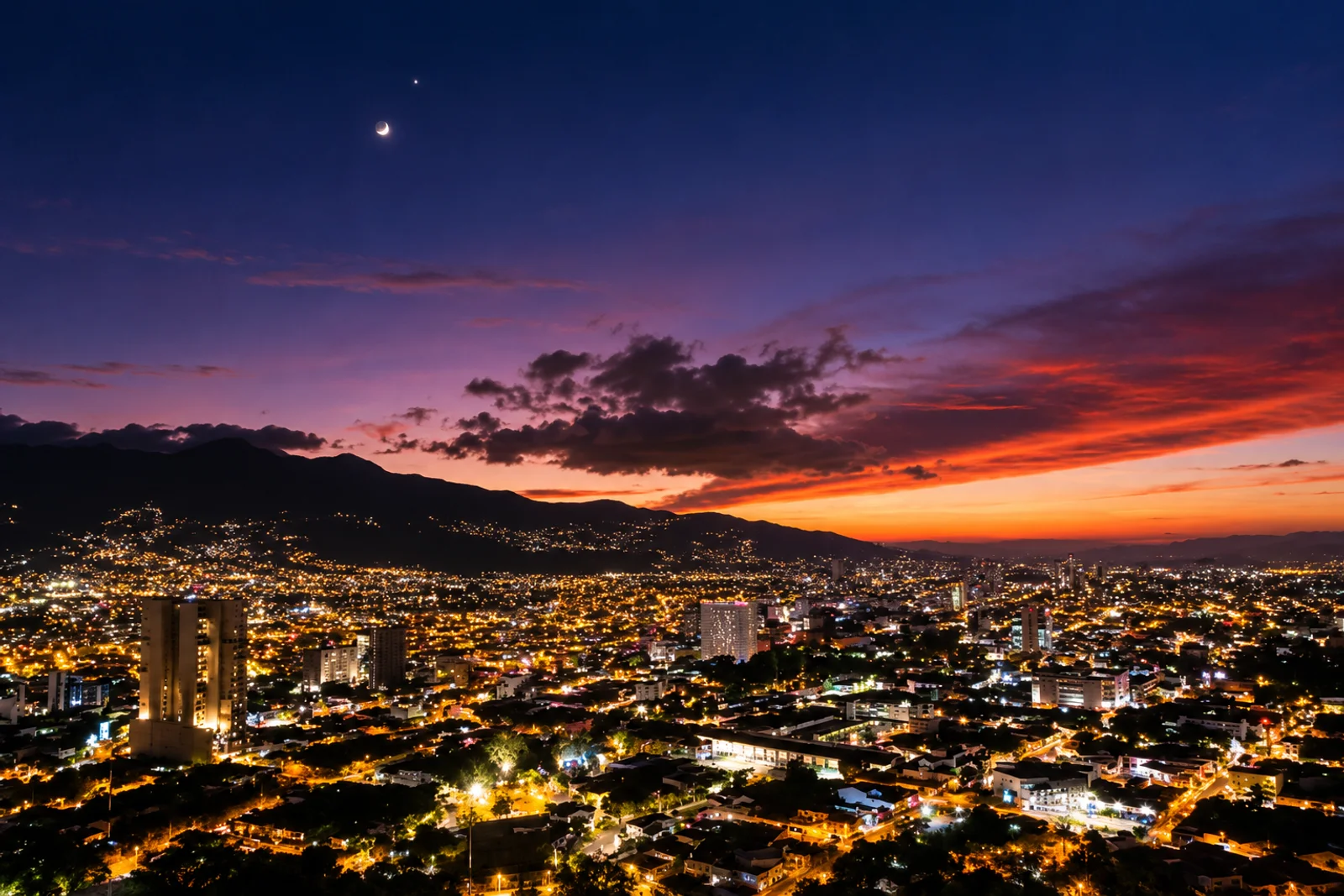 City lights spread across a valley at dusk with mountains and a crescent moon in a colorful sky, San Jose