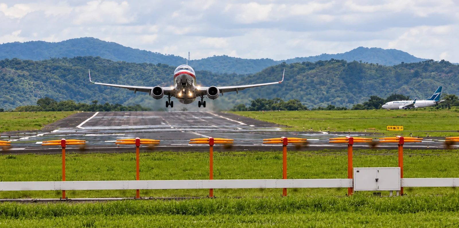 A jet airliner touches down on a runway with forested mountains in the background