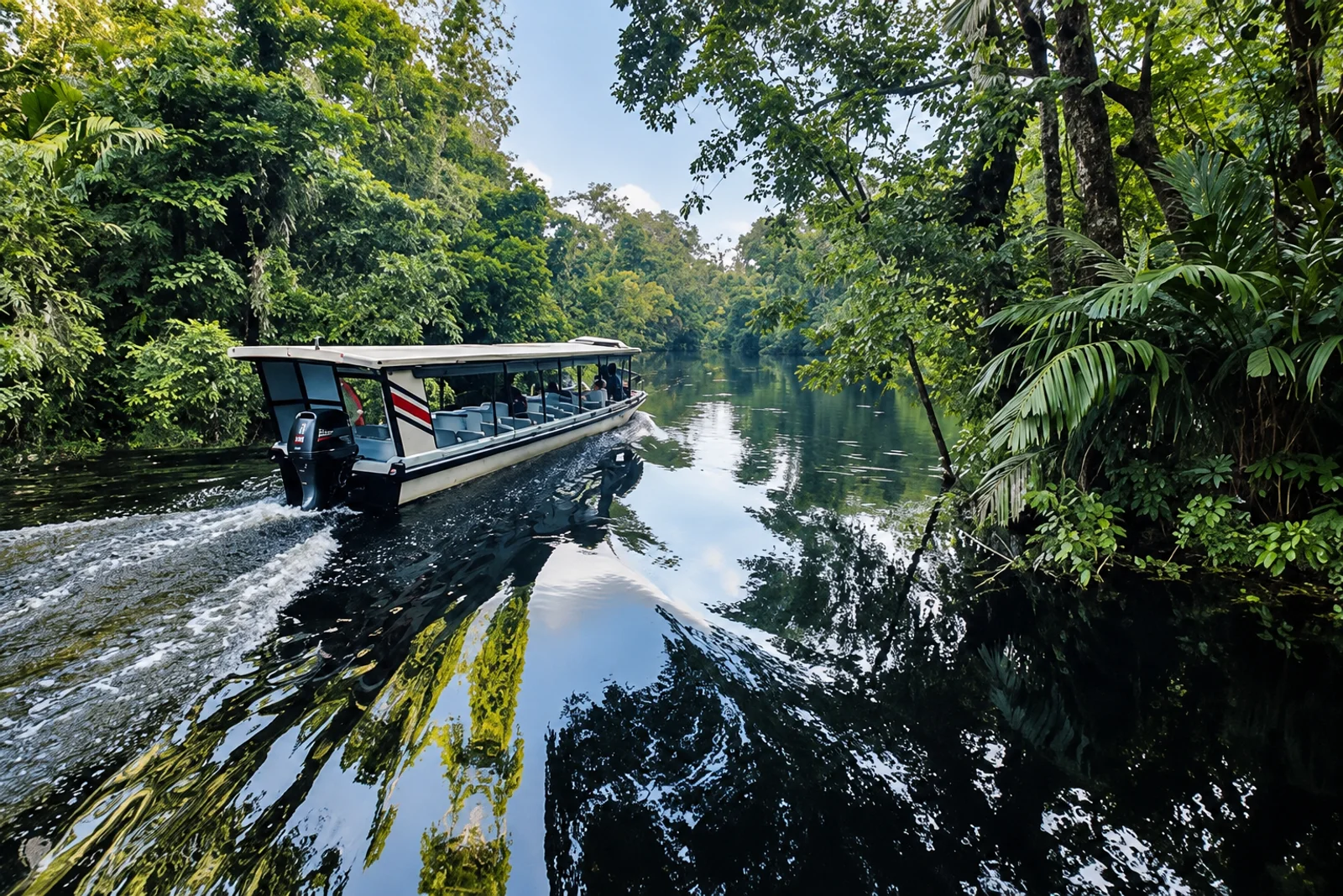 A covered tour boat cruises along a jungle river lined with dense green rainforest