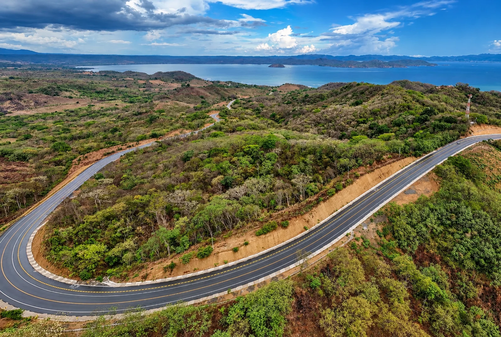 Aerial view of a winding coastal highway curving through green hills above the ocean