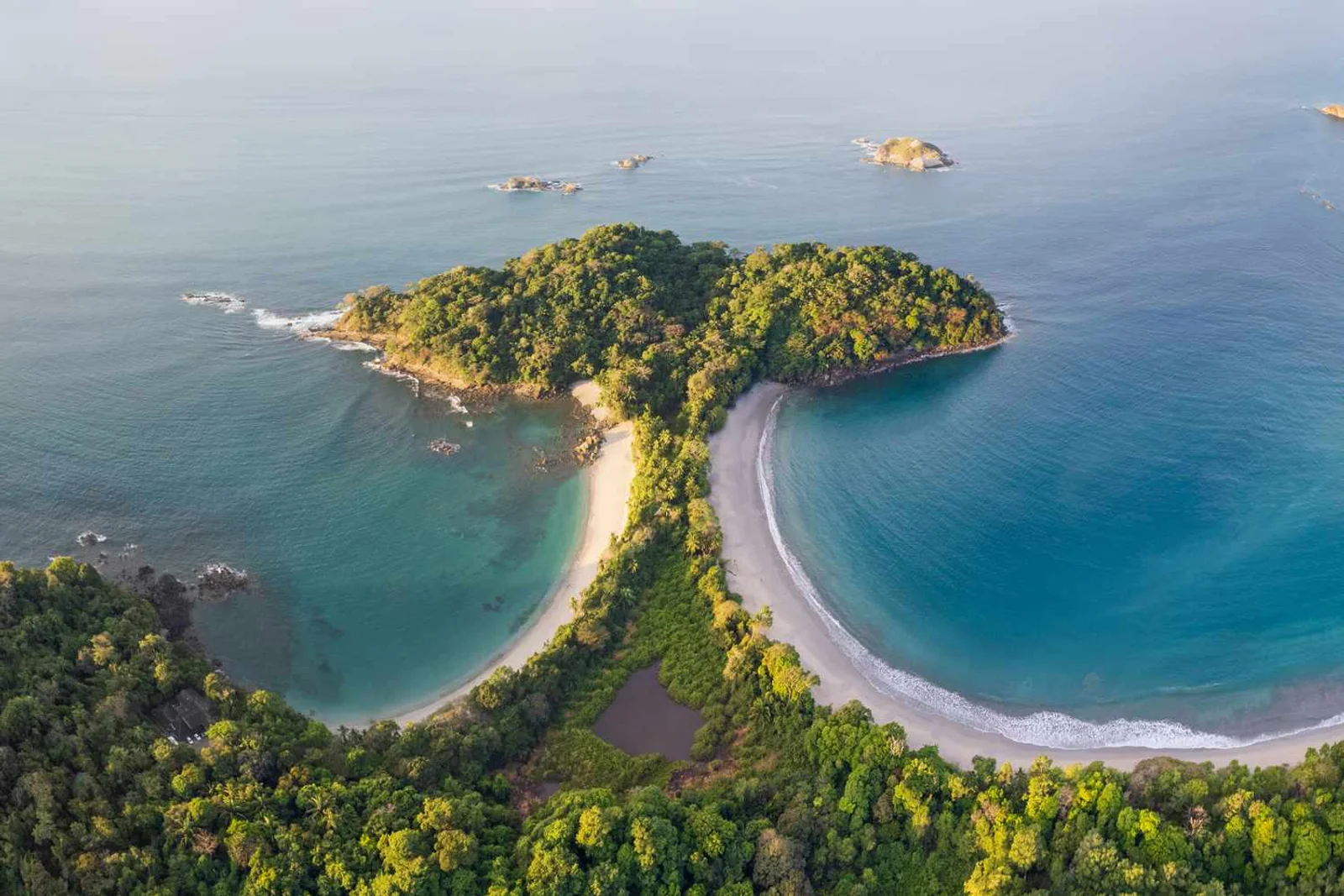 Aerial view of a forested headland in Manuel Antonio with twin sandy beaches and turquoise coves